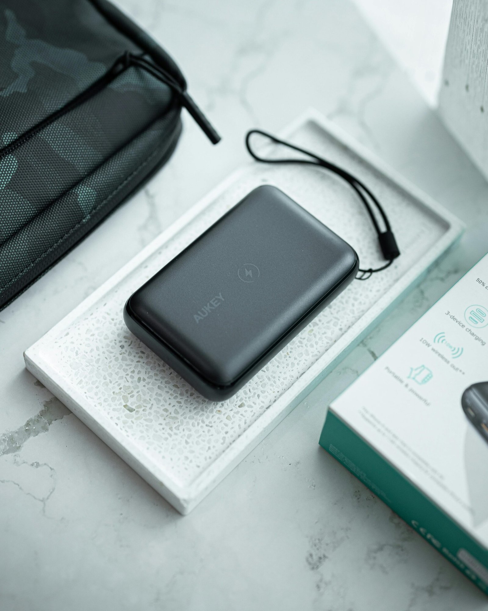 A compact AUKEY wireless power bank placed on a tray next to its product box and a black travel pouch.